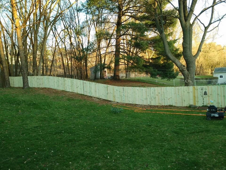 A white wooden fence is surrounded by trees in a backyard.