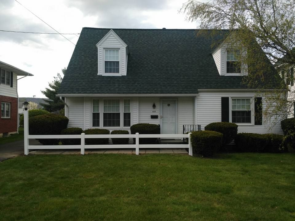 A white house with a green roof and a white fence