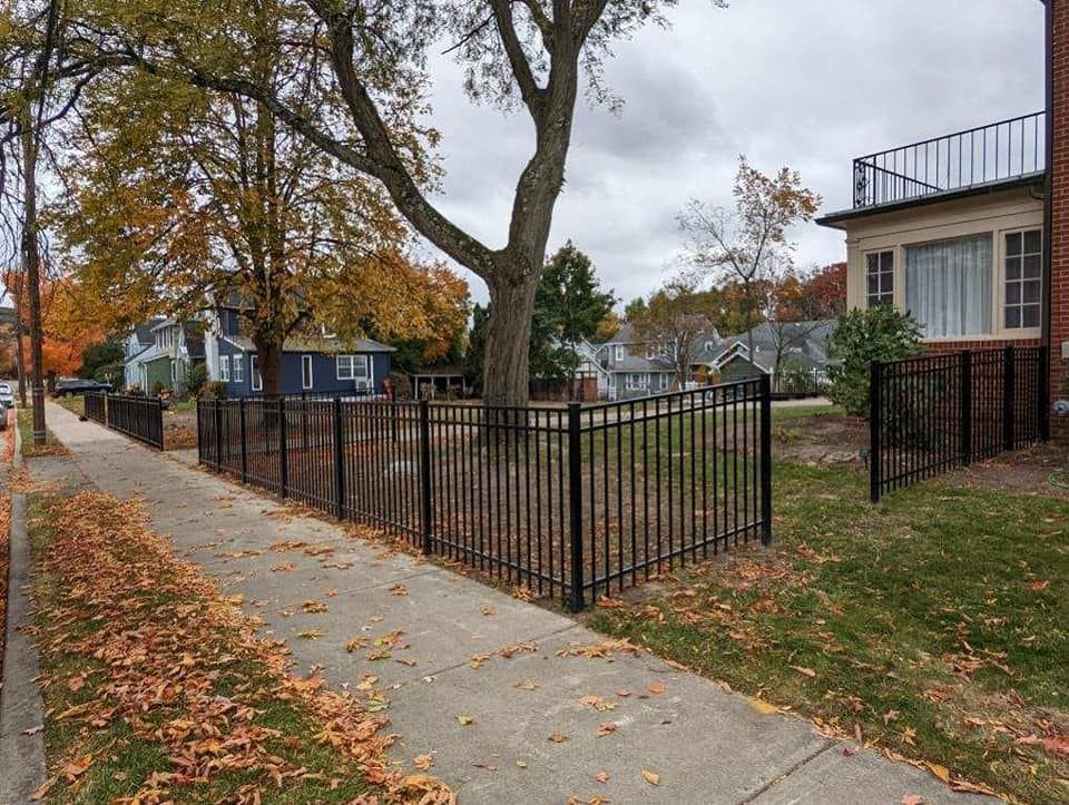 A black fence surrounds a yard in front of a house.