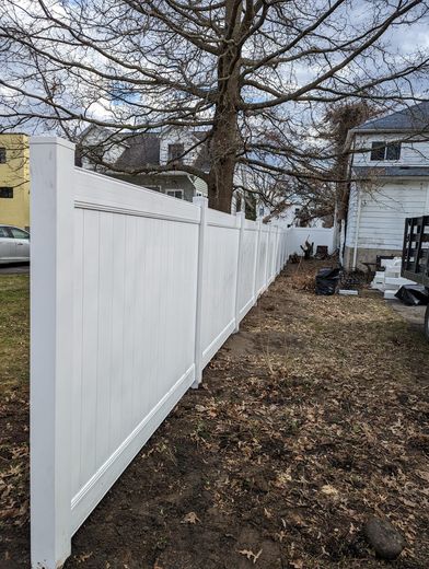 A white fence is sitting next to a tree in front of a house.