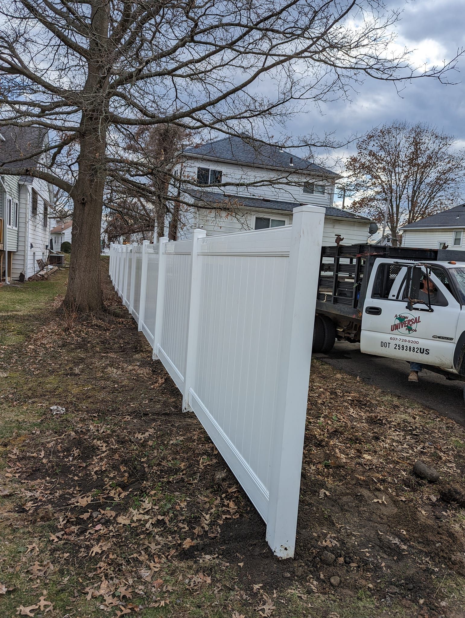 A white truck is parked next to a white fence.