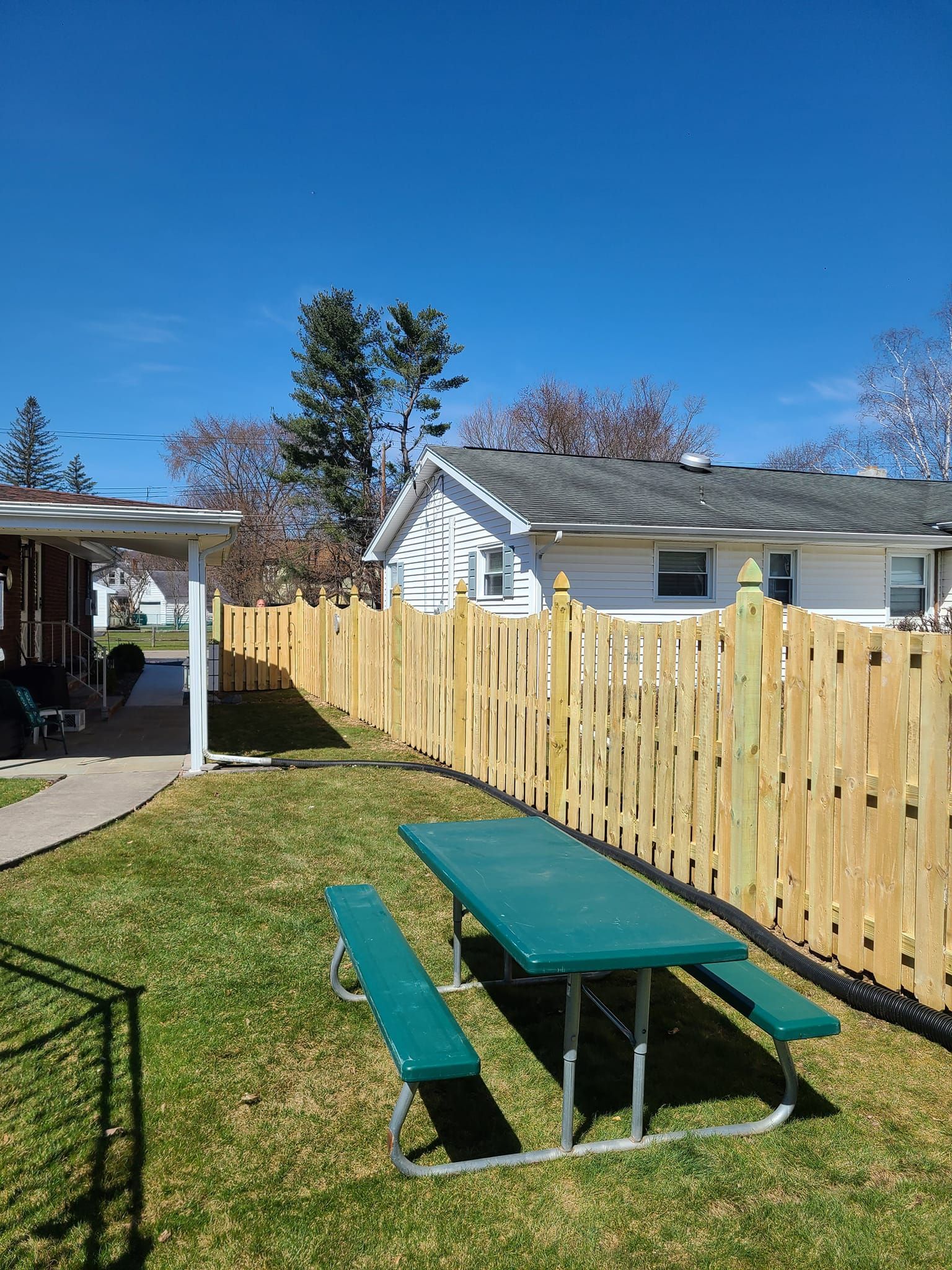 A picnic table and benches in a backyard next to a wooden fence.