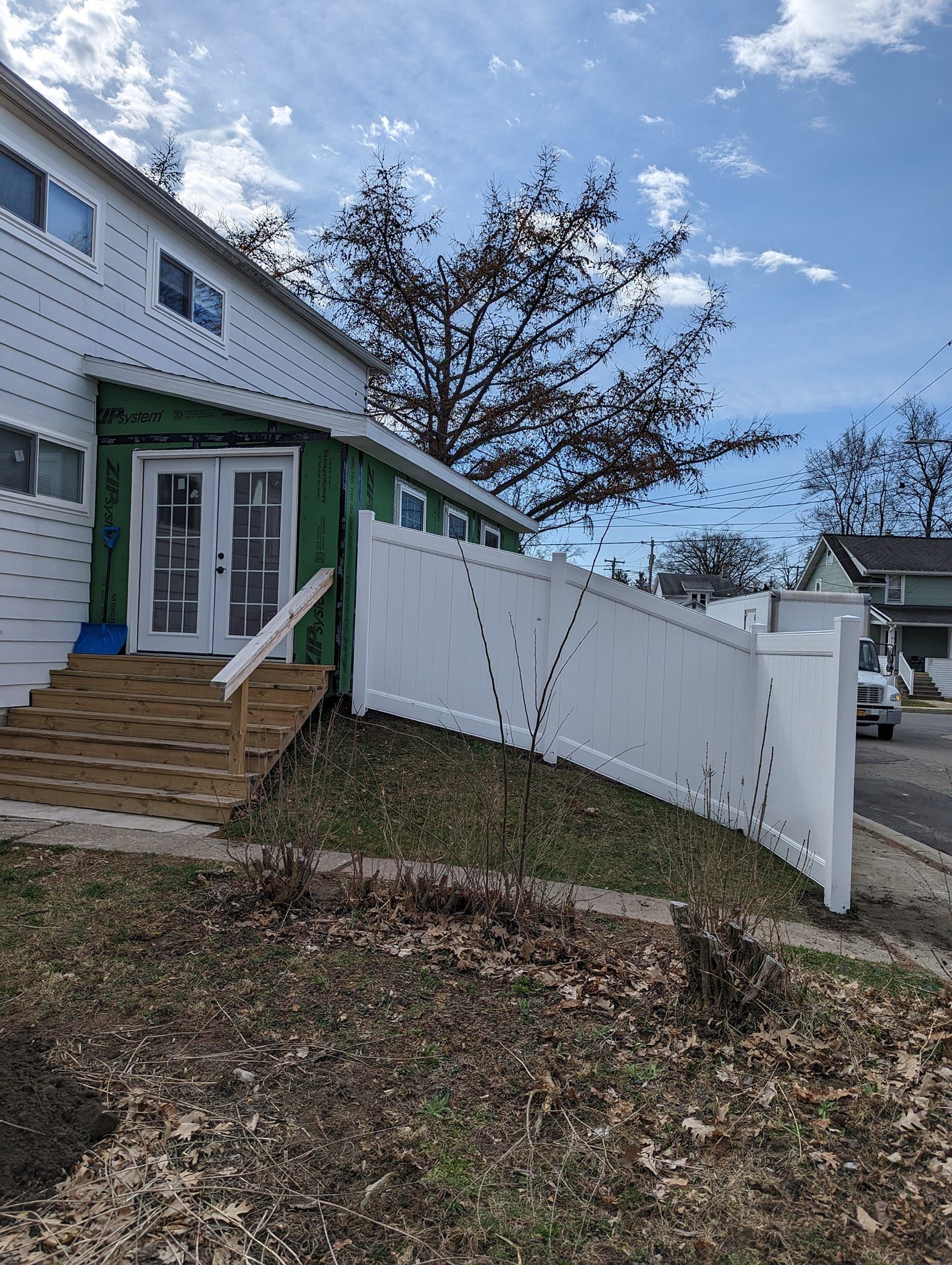 A white fence surrounds a house with stairs leading up to it.