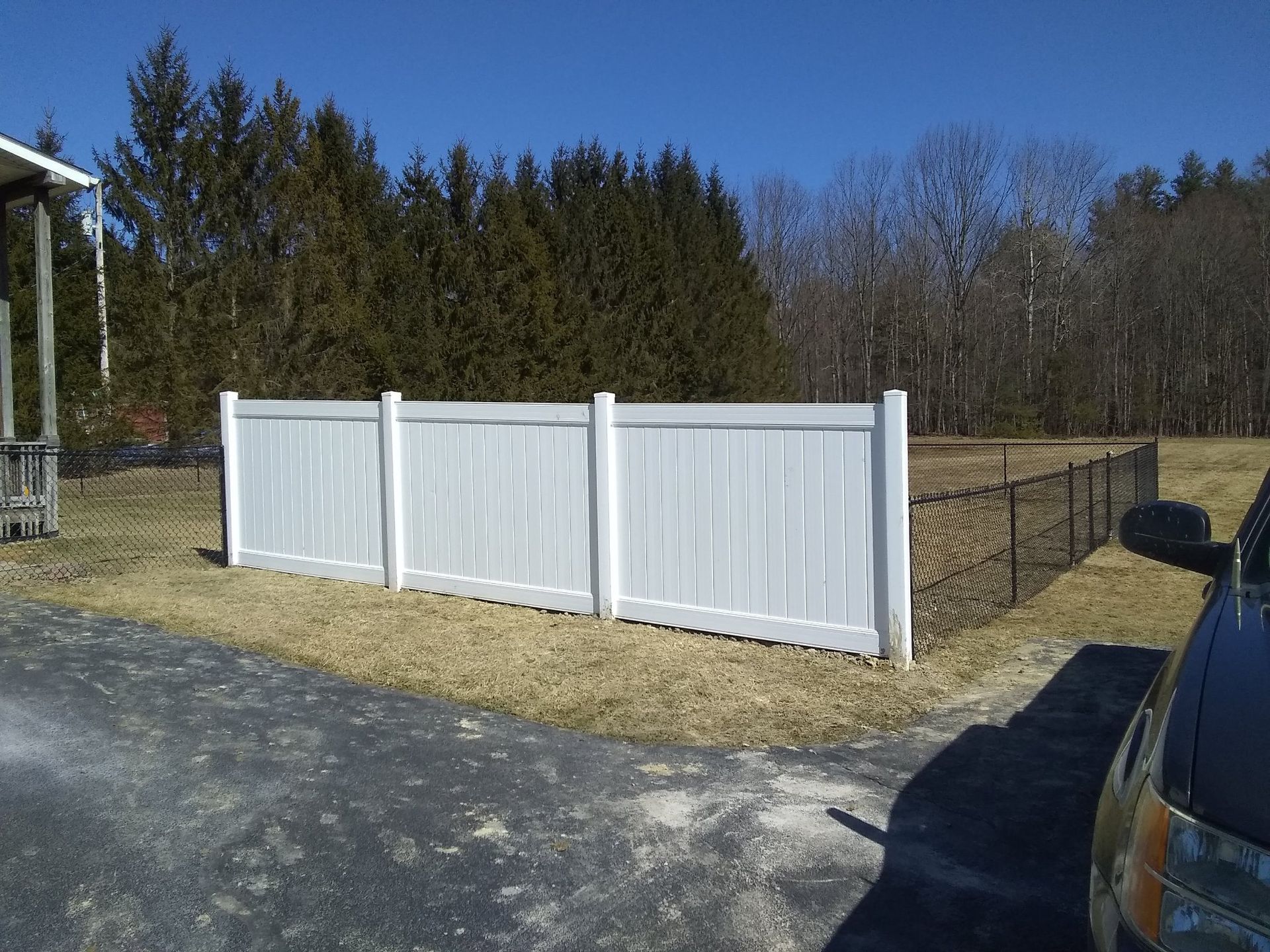 A white fence is sitting on the side of a road next to a car.