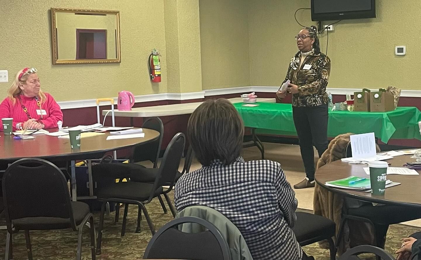 A woman is giving a presentation to a group of people sitting at tables.