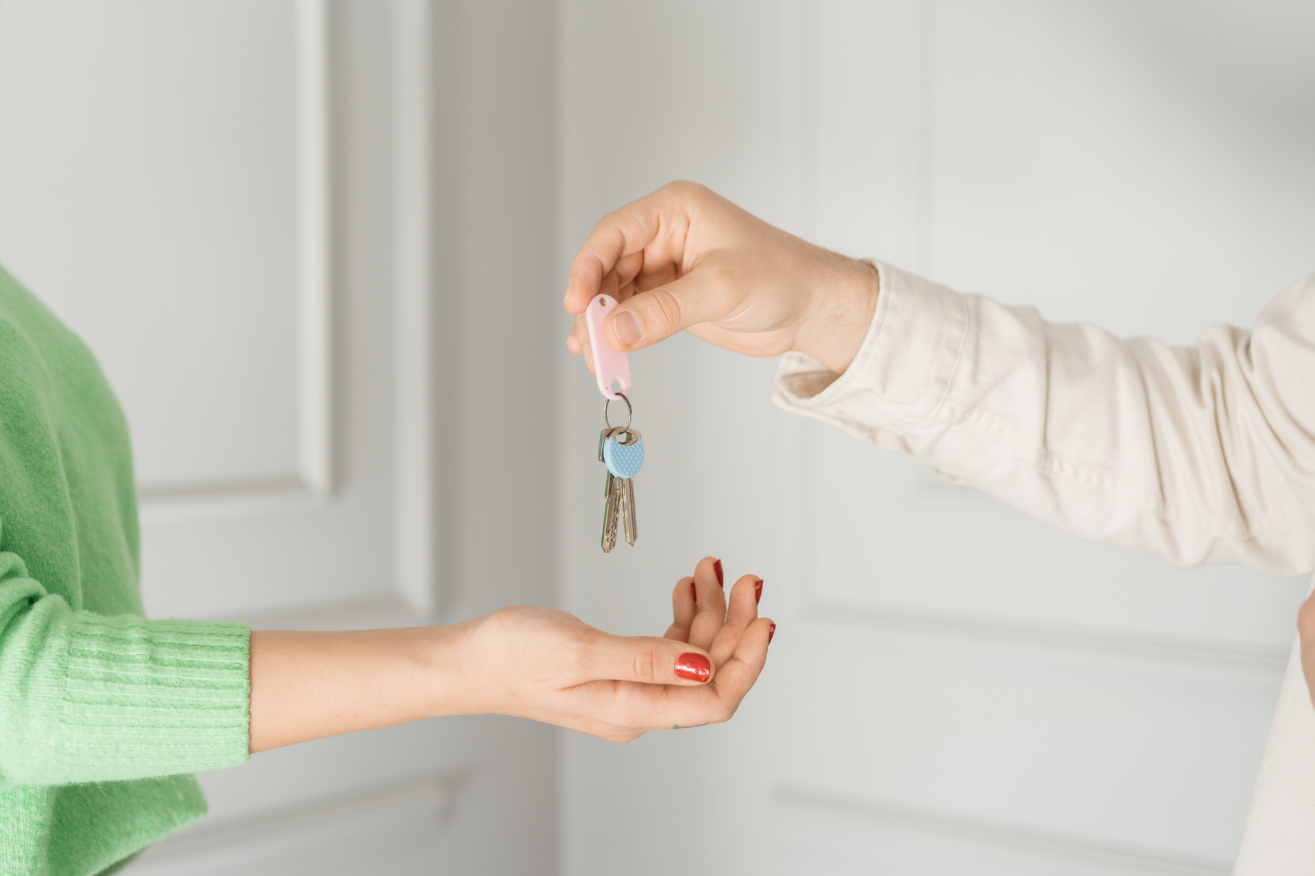 Person handing keys to another person, light-skinned hands, pink key fob, white and green clothing.