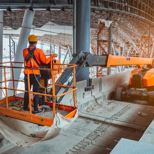 A construction worker is standing on a lift at a construction site.