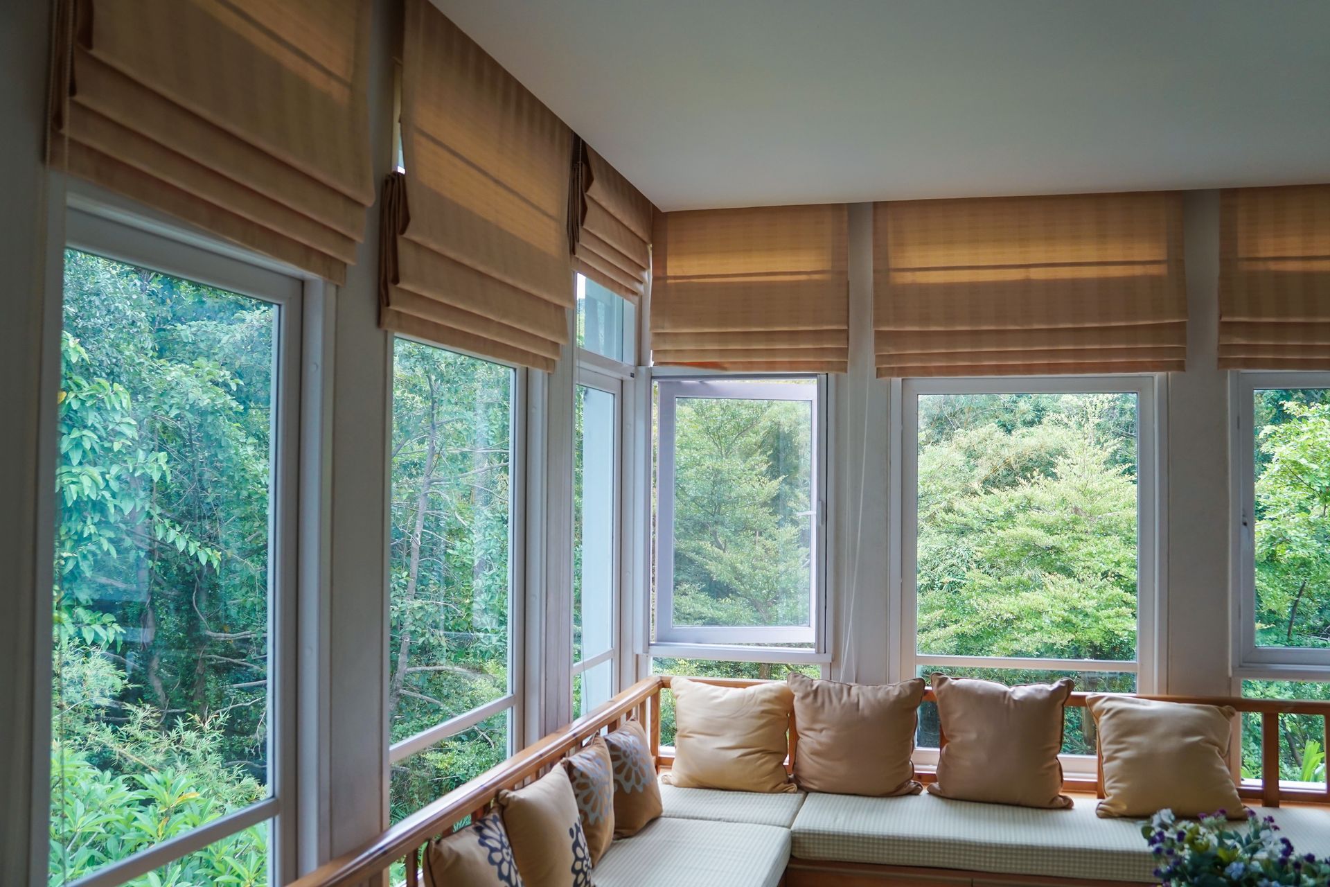 Sunroom with window shades, built-in bench seating, and view of green foliage outside the windows.