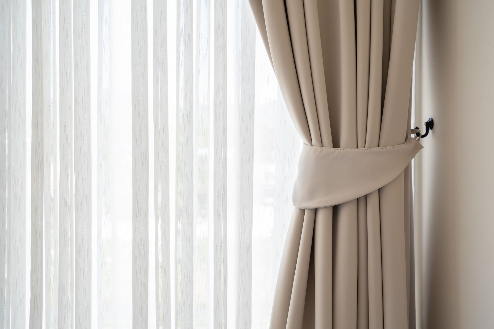 Beige curtains tied back with a matching tieback, sheer white curtains visible behind.