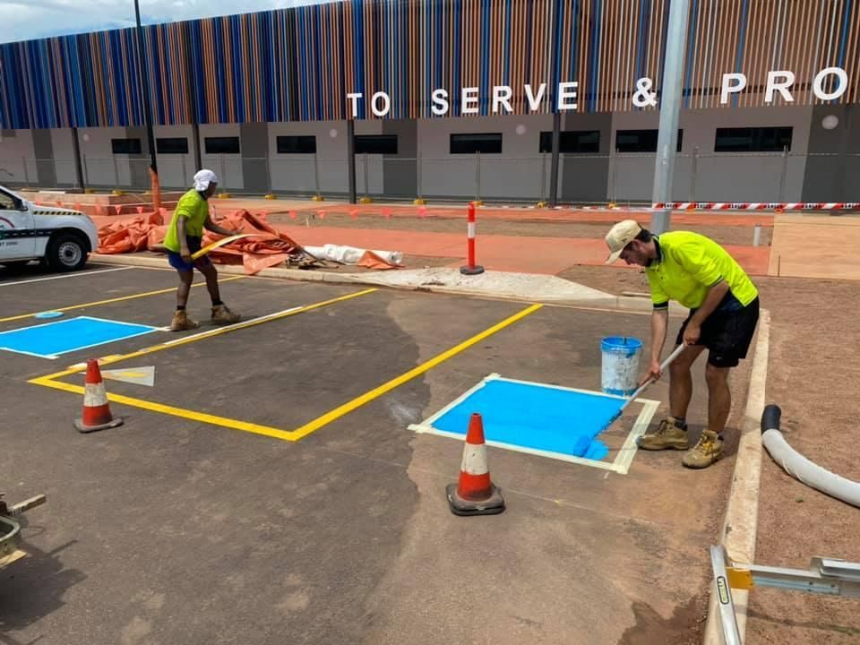 Two Men Are Painting a Parking Lot with Blue Paint — Top End Line Markers Pty Ltd in Katherine, NT