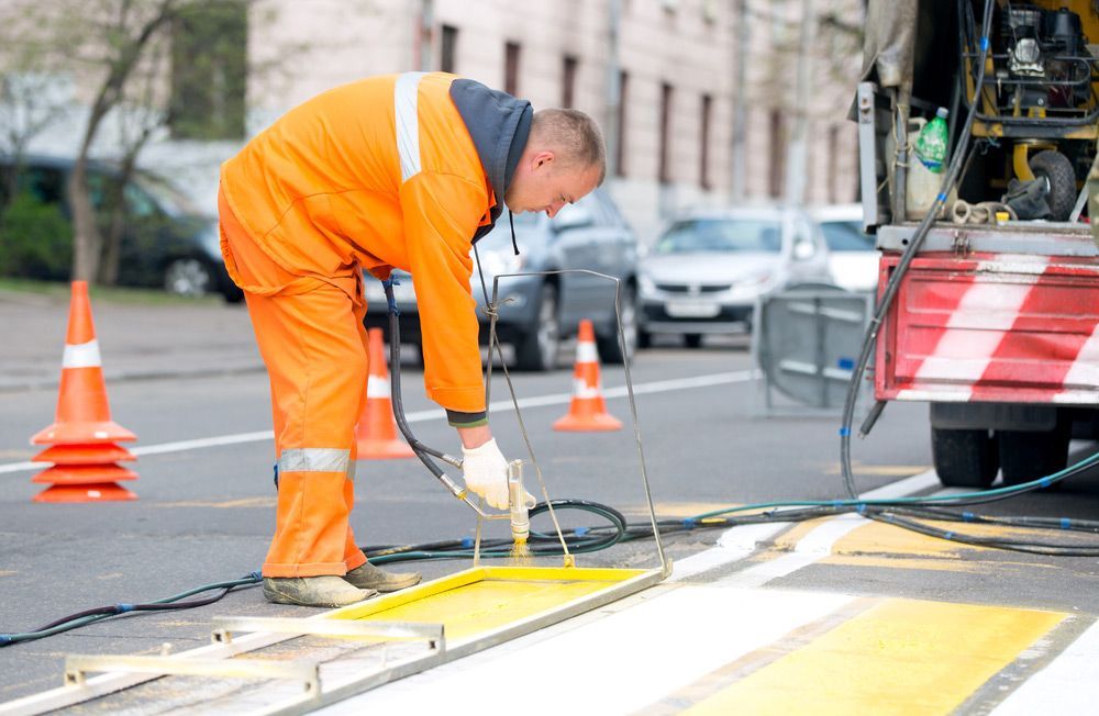 A Man Is Painting a Yellow Line on The Side of A Road — Top End Line Markers Pty Ltd in Katherine, NT