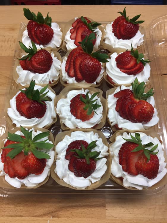 A tray of cupcakes with whipped cream and strawberries on top