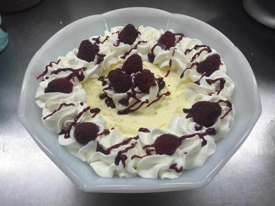 A bowl of ice cream with whipped cream and raspberries on top