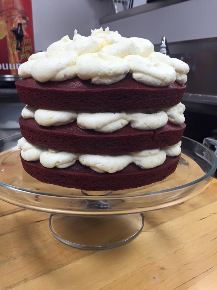 A red velvet cake with white frosting on a glass plate