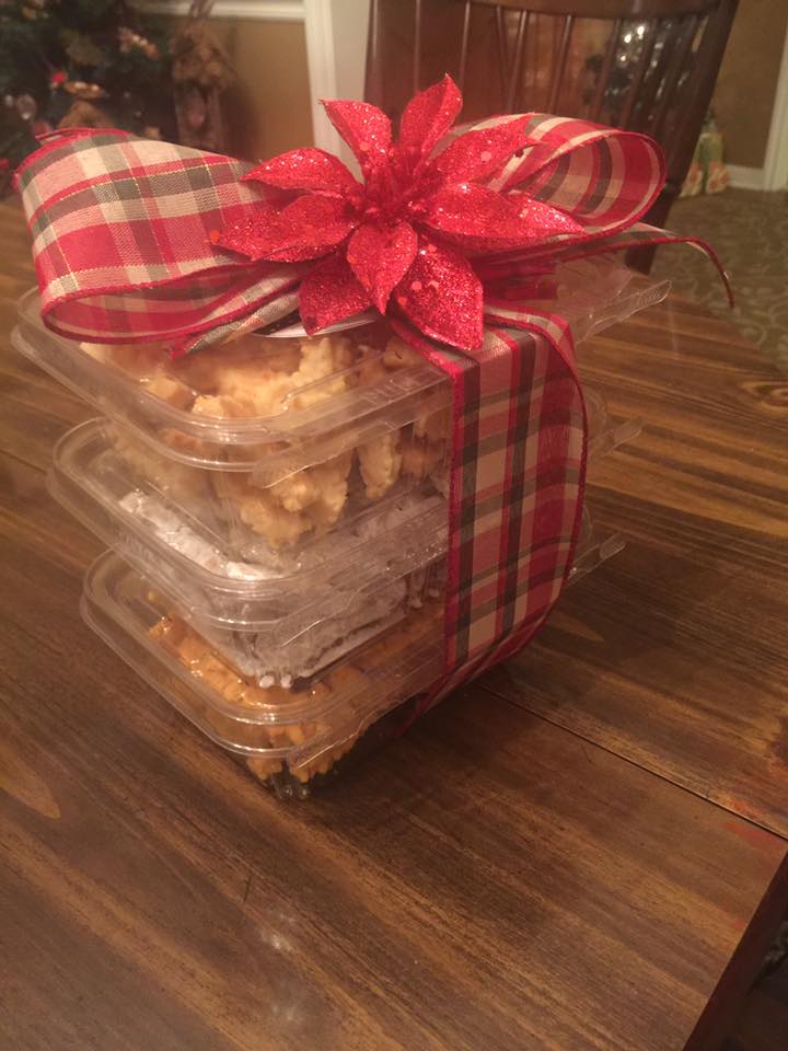 A stack of plastic containers filled with cookies and a red bow on a wooden table.