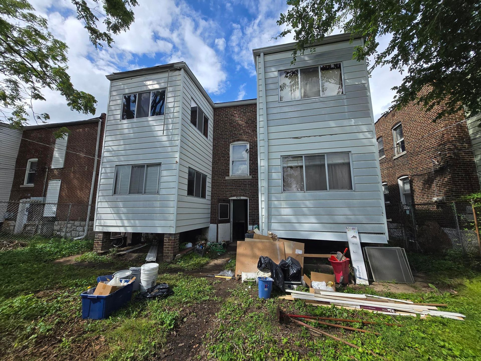 Rear view of two-story buildings in disrepair with peeling paint, debris, and a cloudy sky.