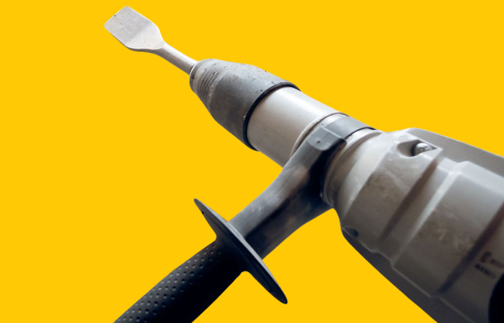 A power drill with a chisel bit, against a yellow background. The drill is gray with a black handle.