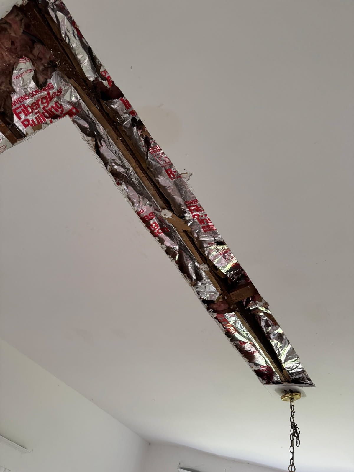 A damaged ceiling with insulation visible in the exposed space. A chandelier hangs below.
