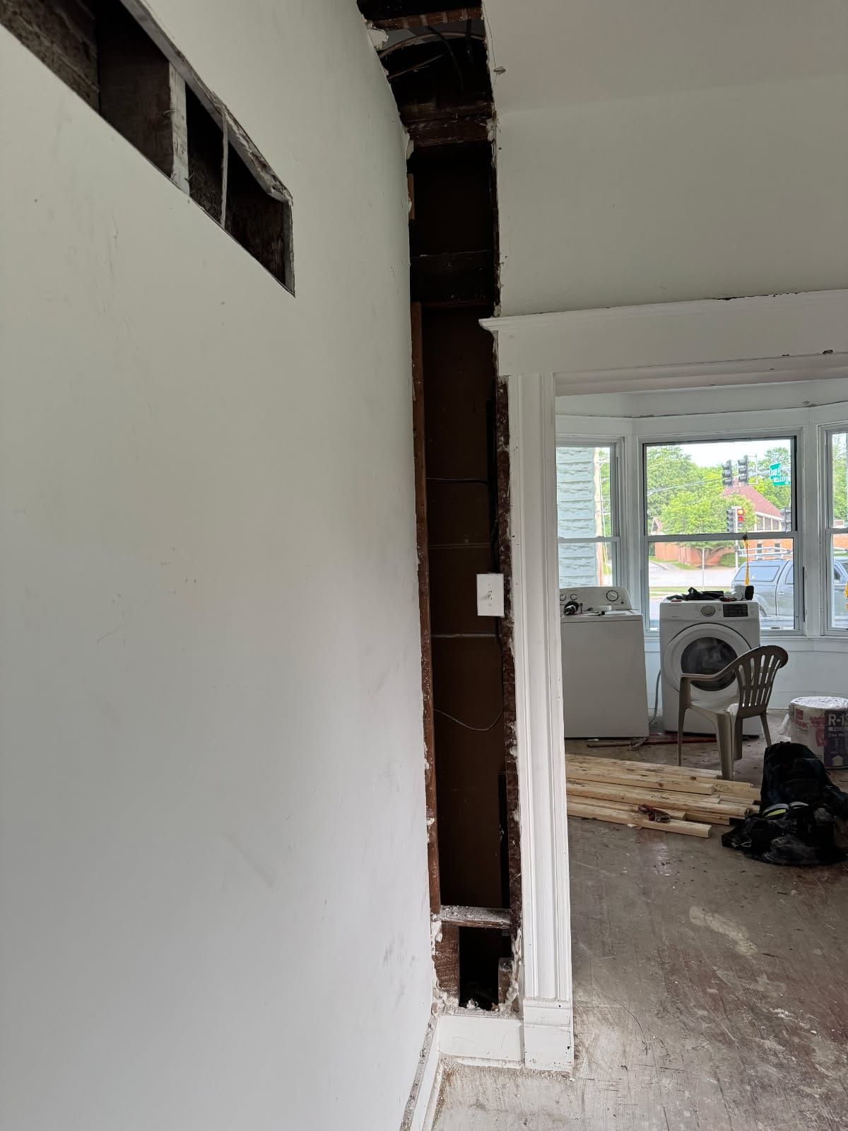 Partial wall with exposed wood and electrical, adjacent to a doorway with white trim. Drywall is present, and a washing machine is visible.