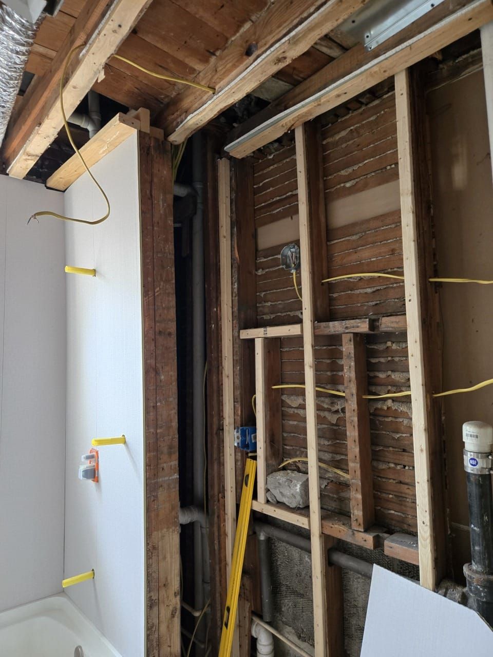 Bathroom under renovation: Exposed wall studs, pipes, wiring, and unfinished drywall. A level and lighting fixtures are also visible.