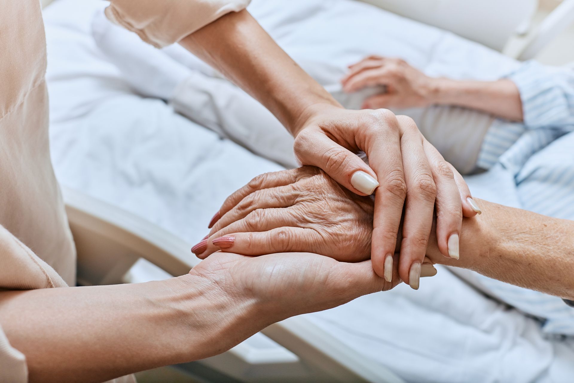 Person holding the hand of an elderly person in bed; offering comfort and support.