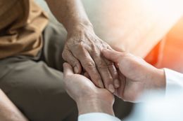 A person's hand held by another person's hand; offering comfort and care, lit by sunlight.