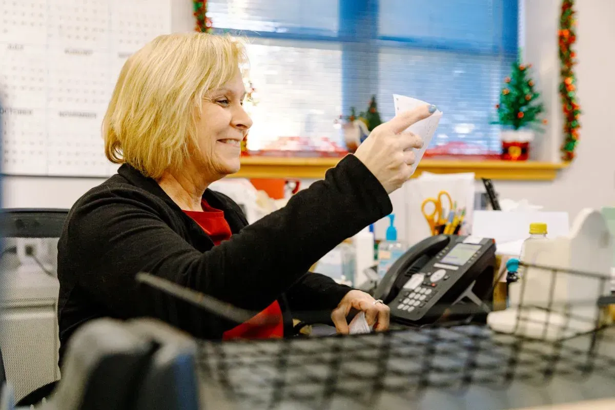 A woman is sitting at a desk holding a piece of paper.