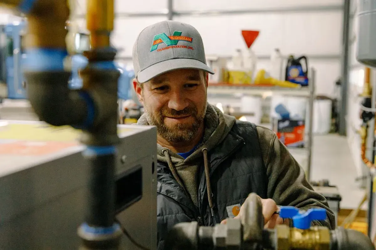 A man in a hat is working on a pipe in a garage.