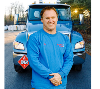 A man in a blue shirt is standing in front of a blue truck with a 1073 sign on it