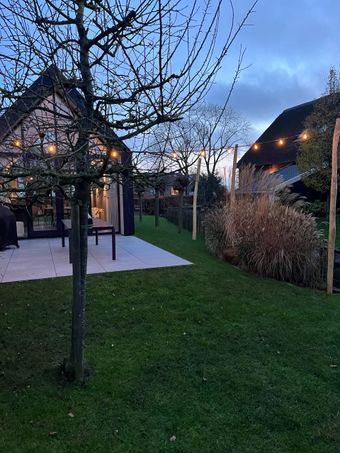 Nachtopname van een huis met lichtslingers en hoog siergras ervoor.