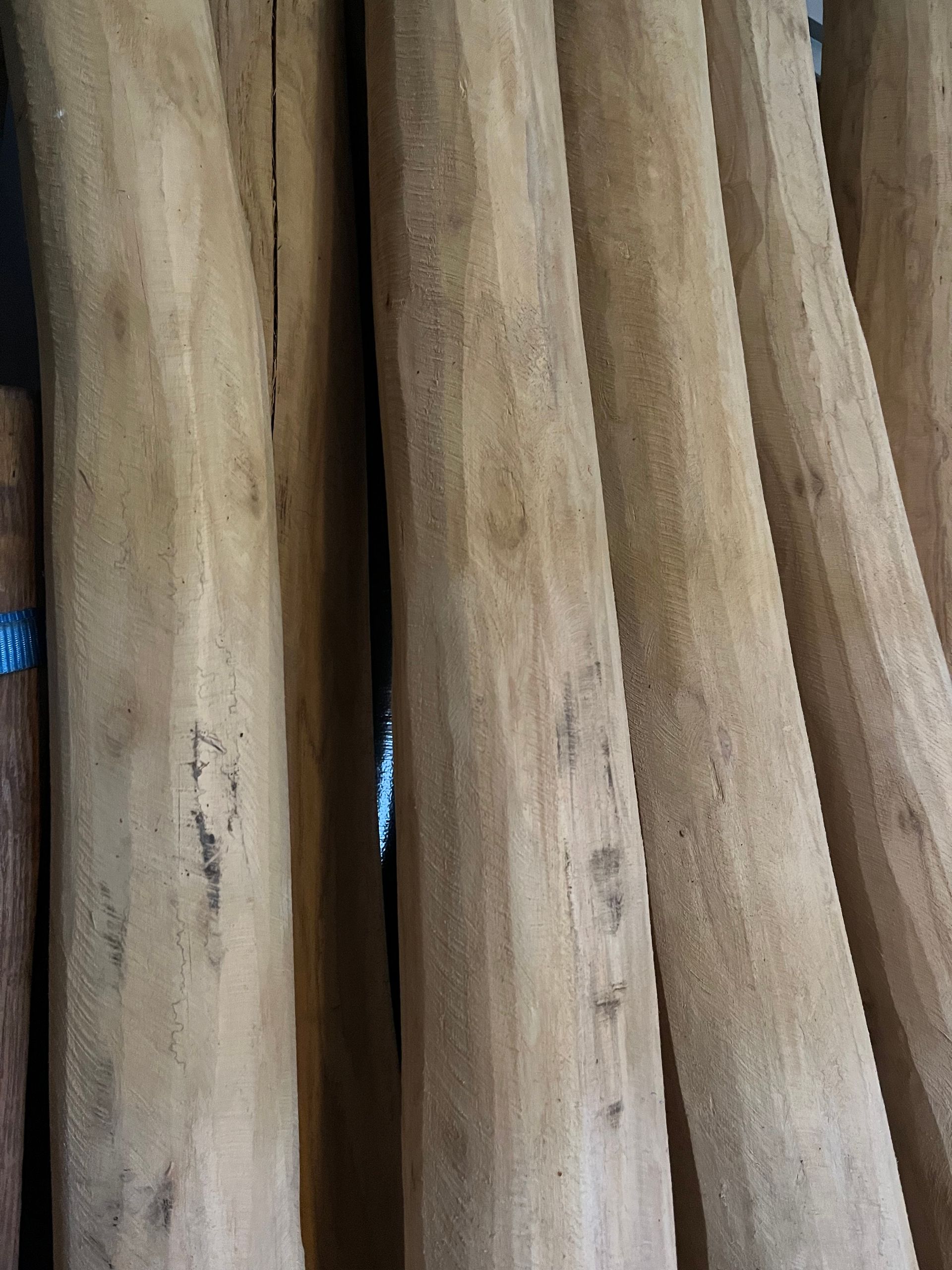Verticaal gestapelde houten palen, met een natuurlijke lichtbruine kleur, zichtbare houtnerf en lichte imperfecties.
