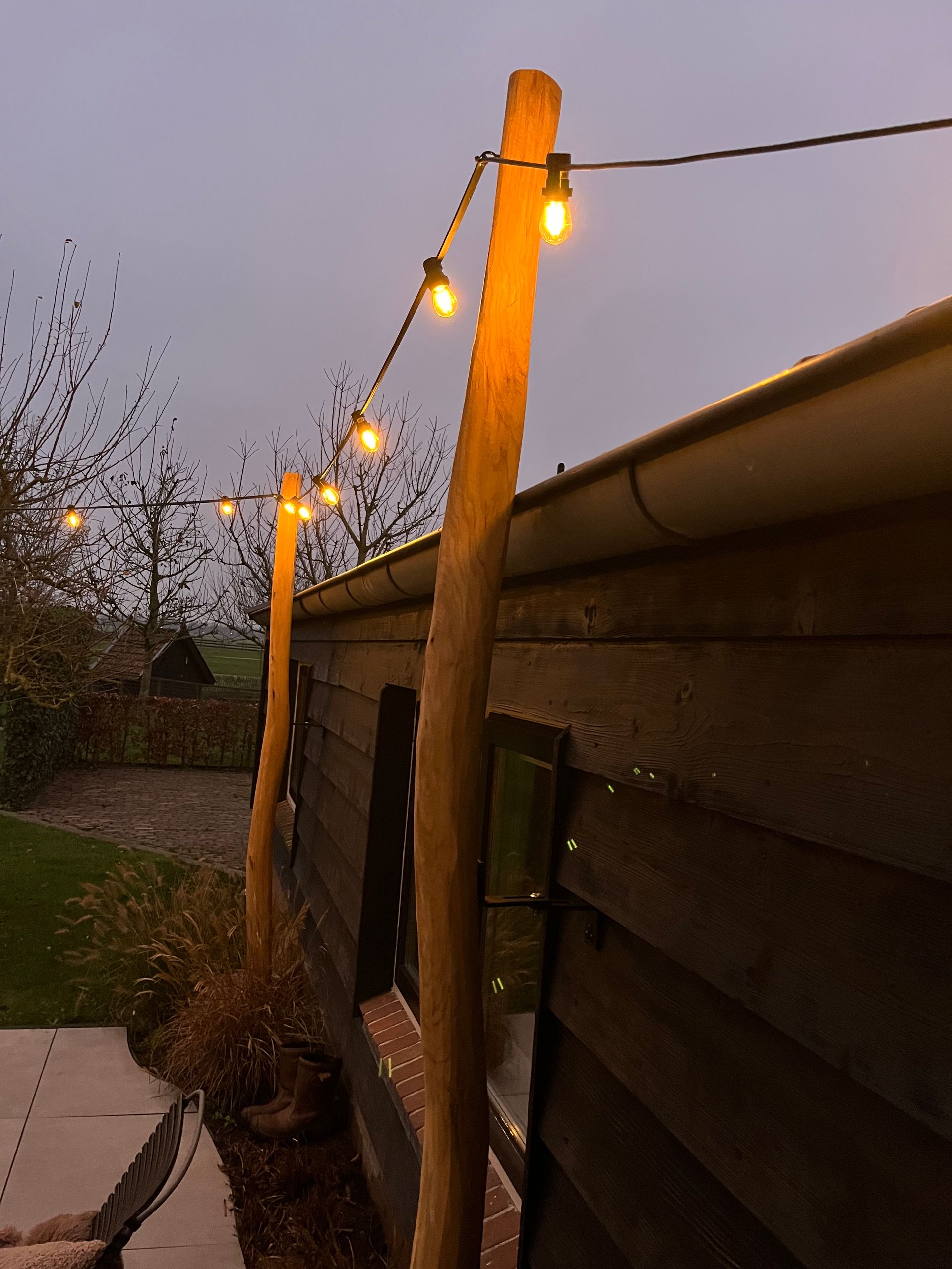 Slingerlampjes aan een houten paal verlichten een grasveld in de schemering.