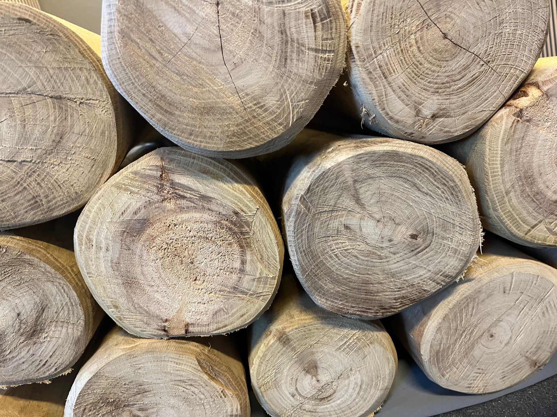 Close-up van een stapel verweerde, lichtbruine houten boomstammen met zichtbare groeiringen.