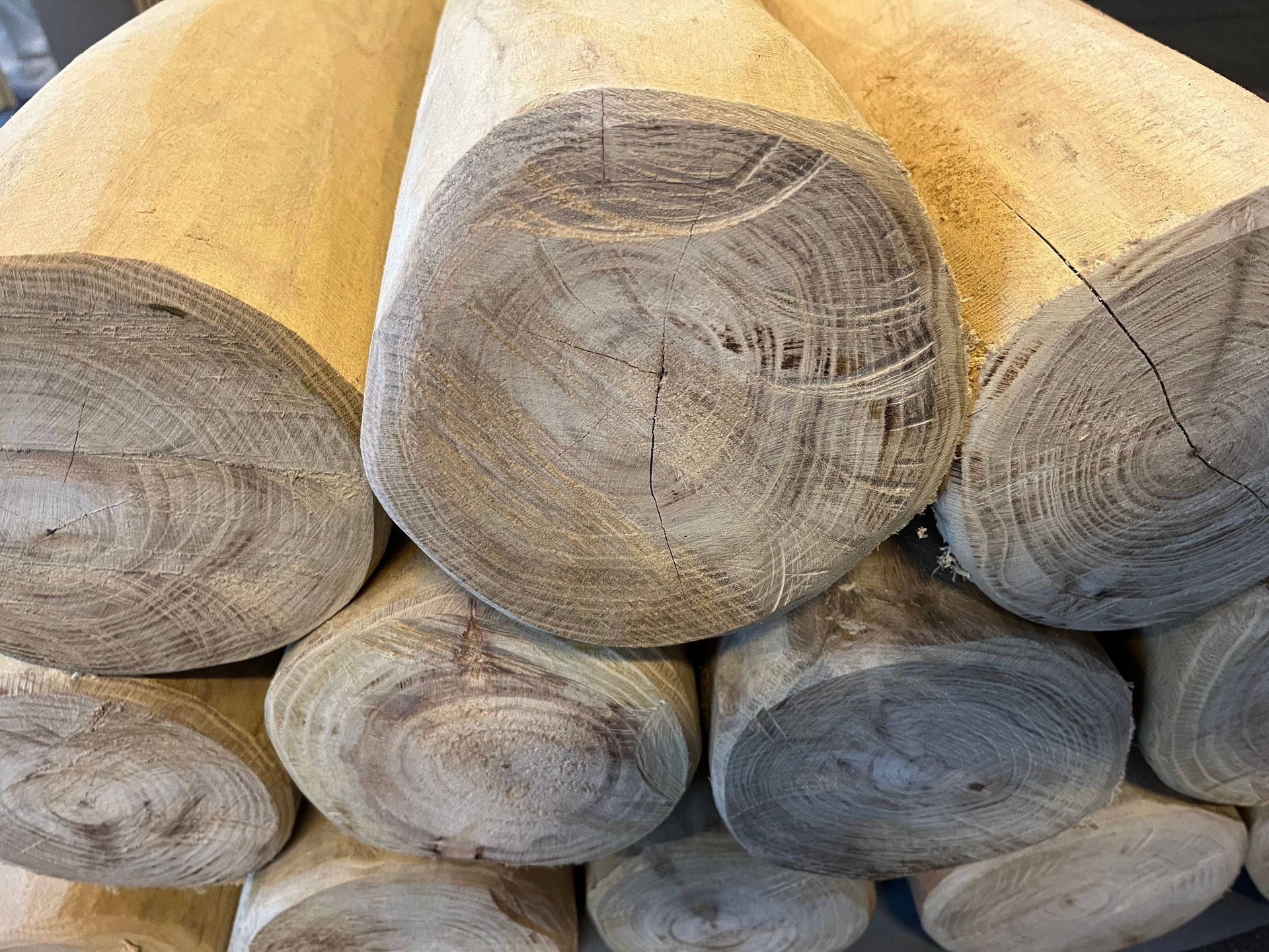 Close-up van een stapel verweerde houten boomstammen, met ronde uiteinden waarop groeiringen en een ruwe bast te zien zijn.