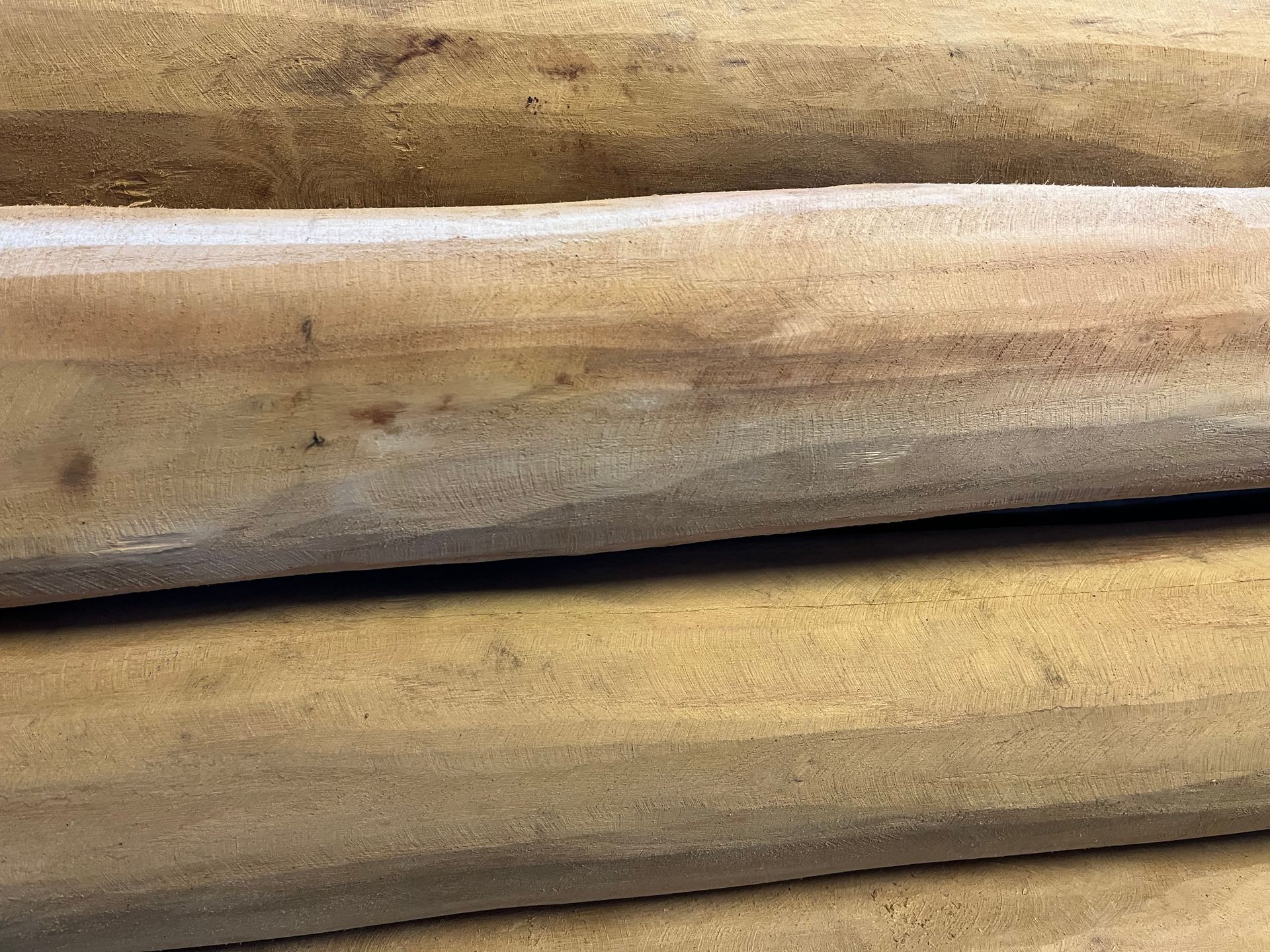 Detailopname van verschillende ruw bewerkte, cilindrische houten balken die horizontaal op elkaar gestapeld zijn en een gevarieerde houtnerf en beigetinten laten zien.