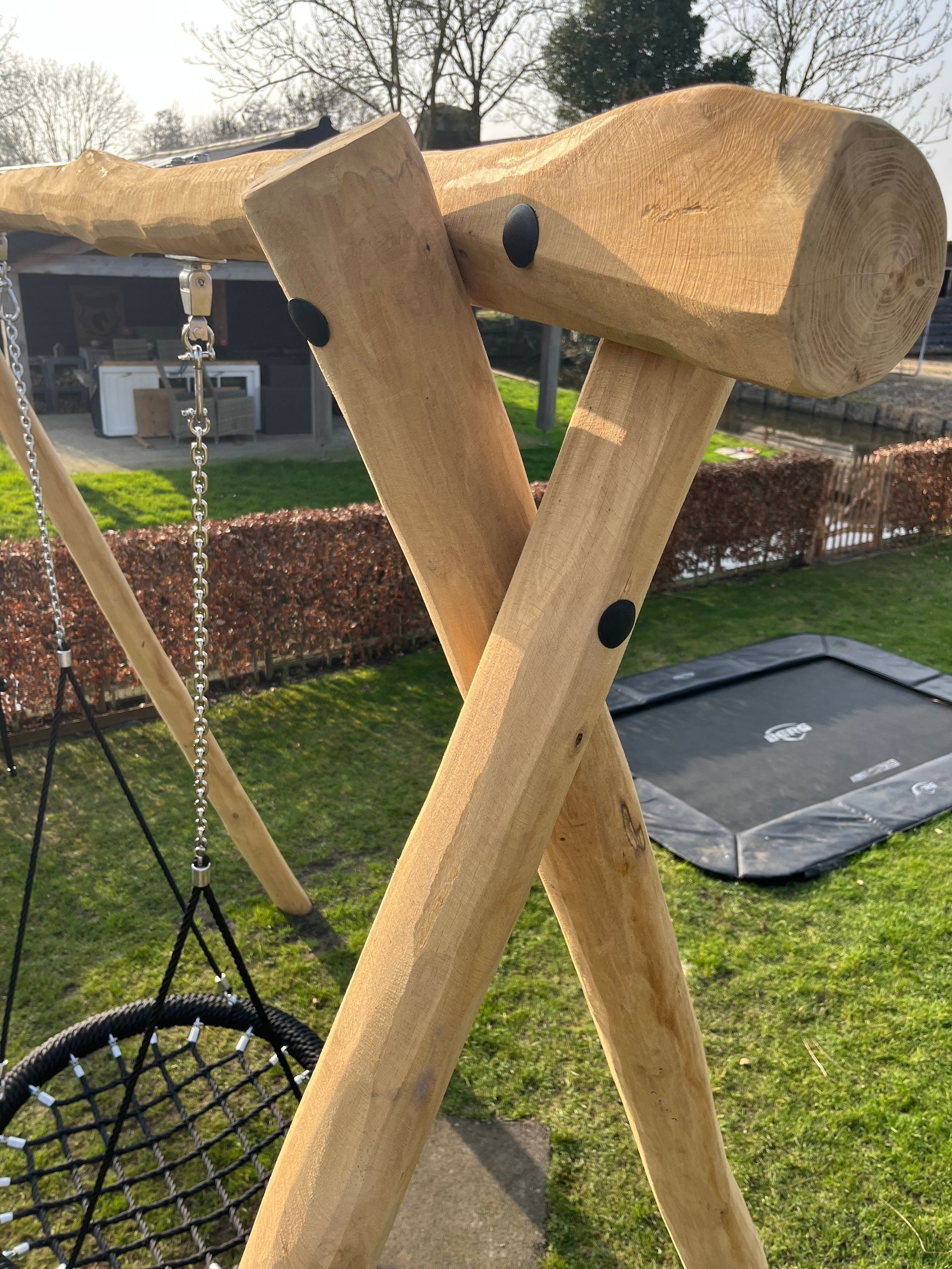 Grijze metalen stang bevestigd aan een boom, met een speeltuin op de achtergrond.