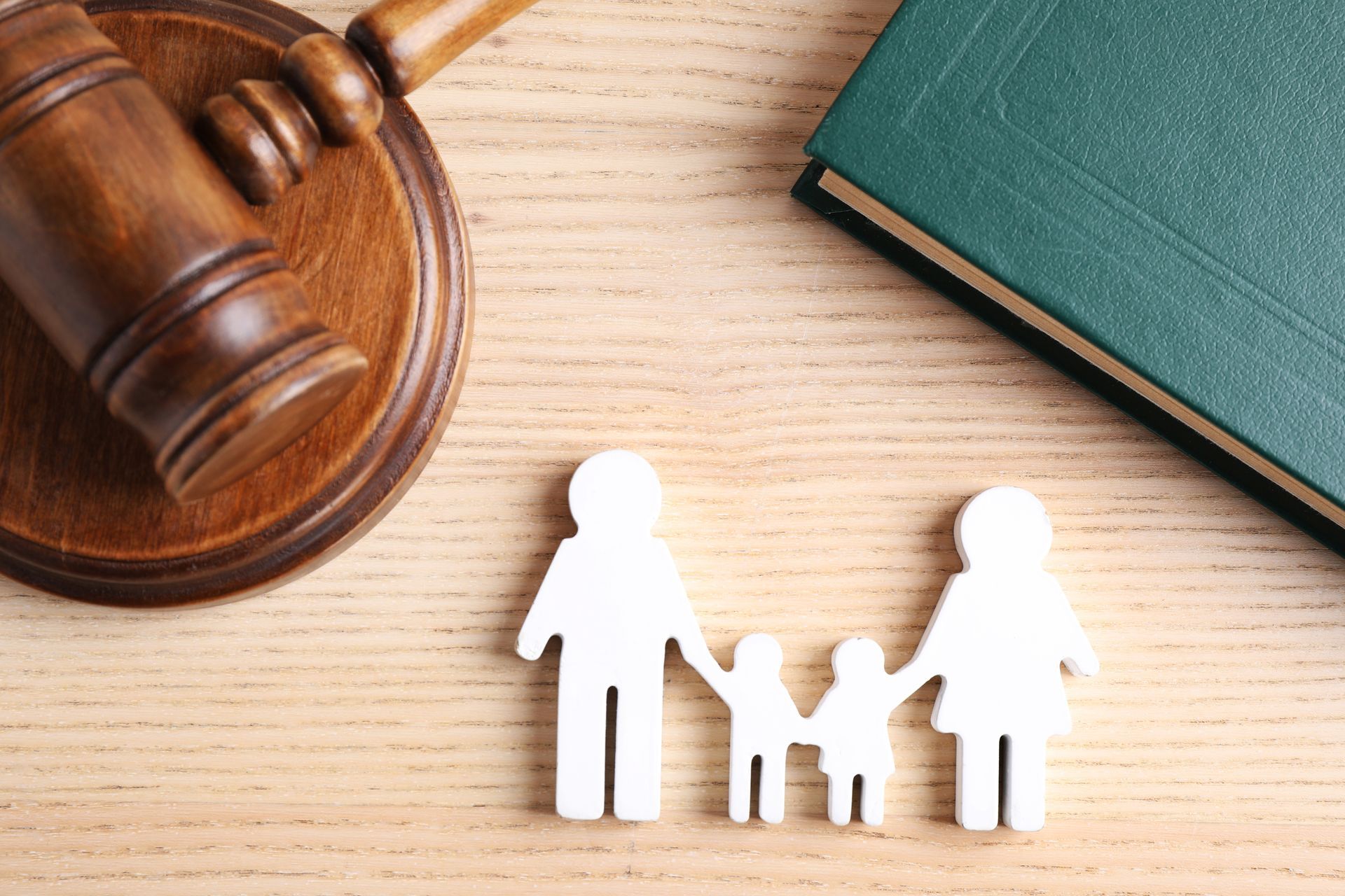 A wooden gavel , a book , and a family cut out of paper on a wooden table.