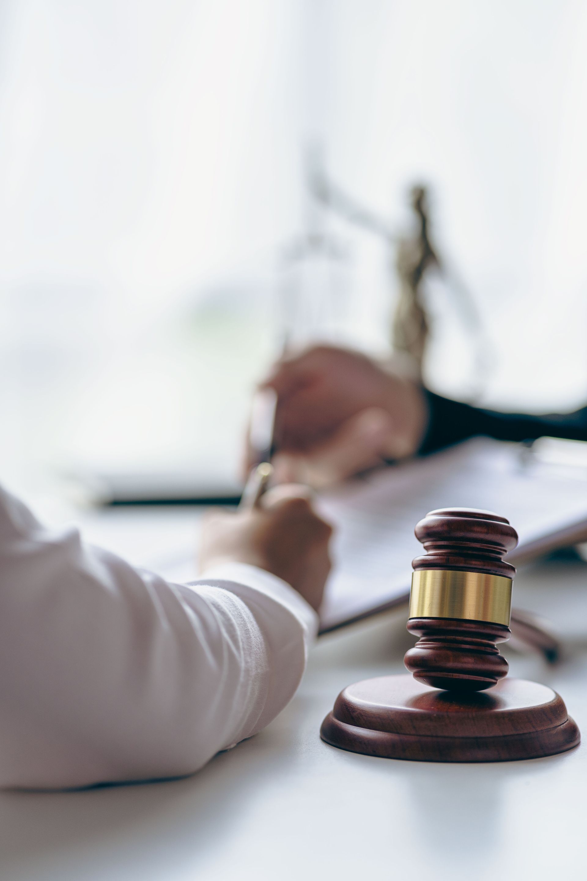 A judge 's gavel is sitting on a table next to a person writing in a notebook.