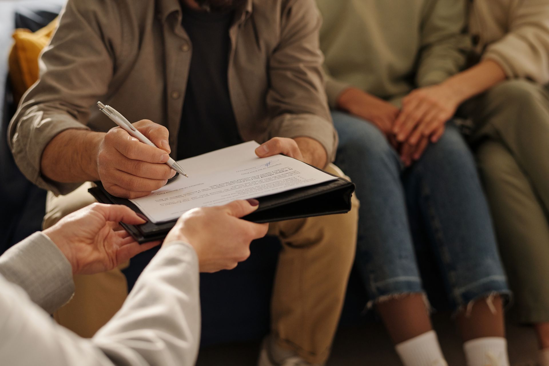 A group of people are sitting on a couch and a man is writing on a clipboard.