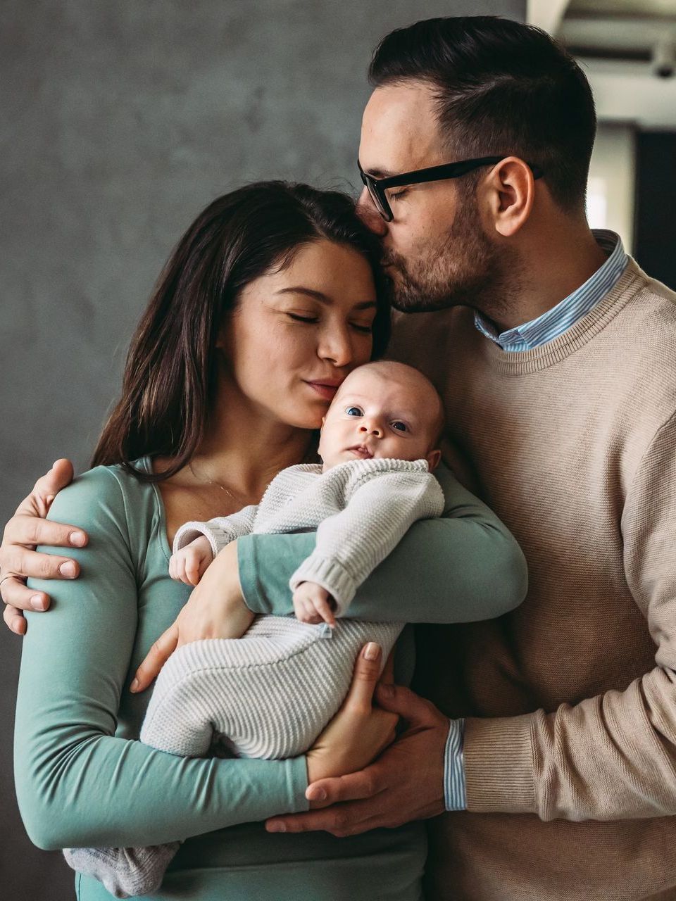 A man is kissing a woman on the cheek while holding a baby.