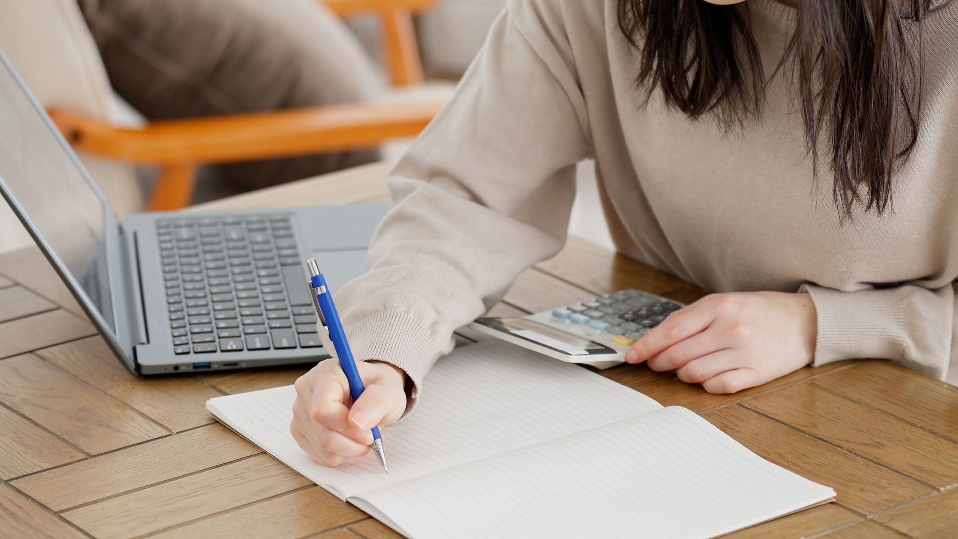 A woman is sitting at a table with a laptop and a calculator.