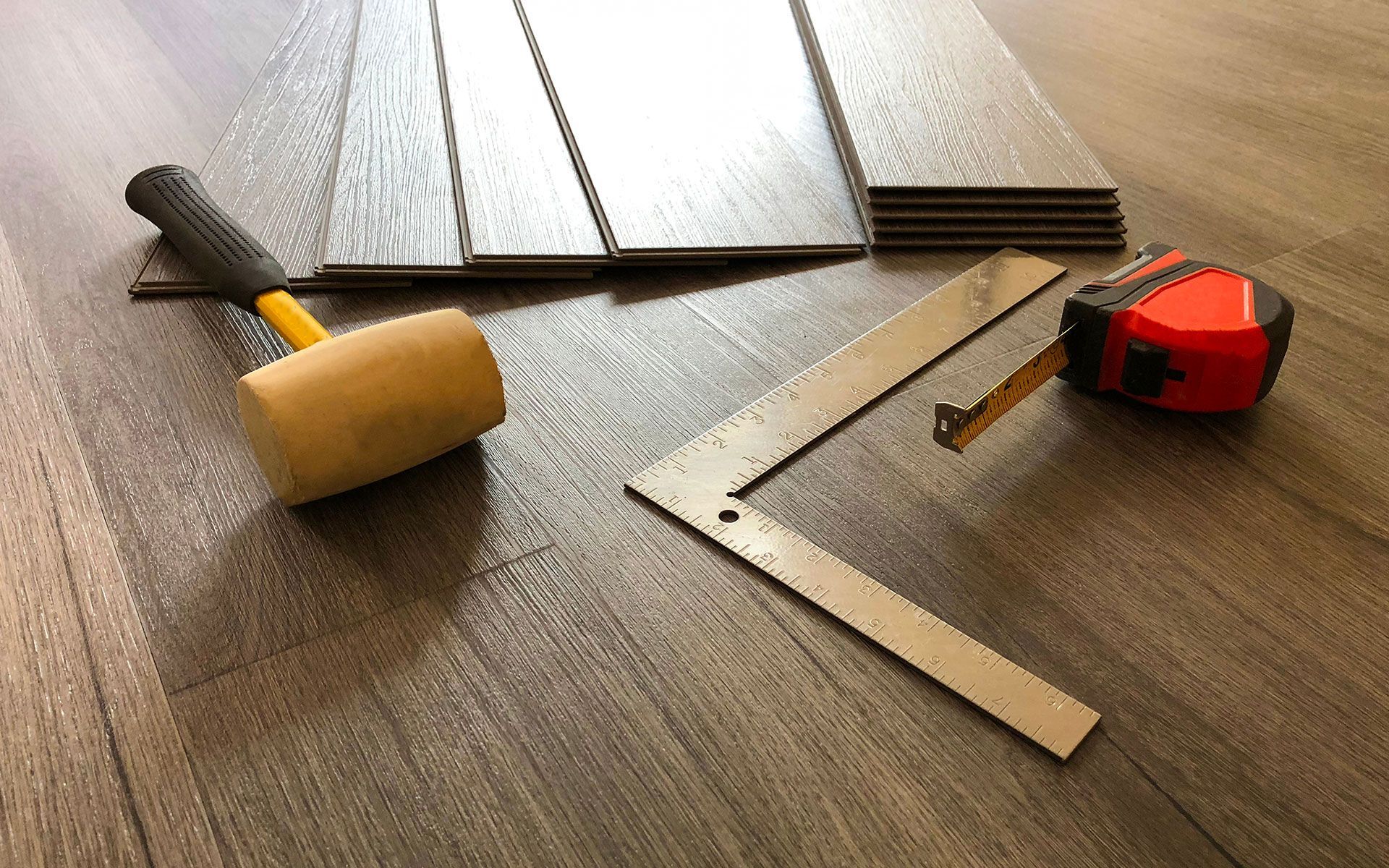 A hammer , ruler , and tape measure are on a wooden floor.