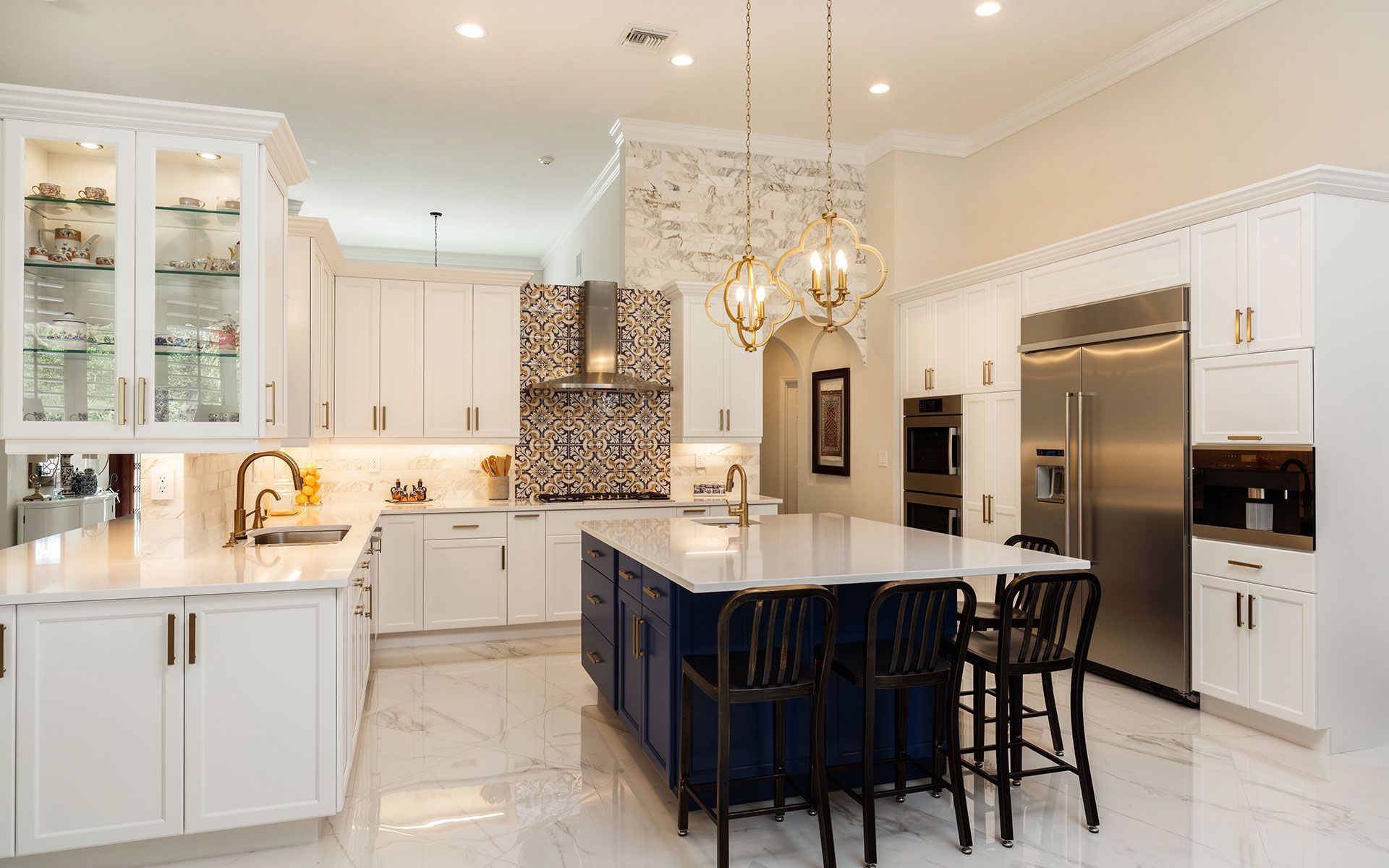 A kitchen with white cabinets , stainless steel appliances , a large island , and a chandelier.
