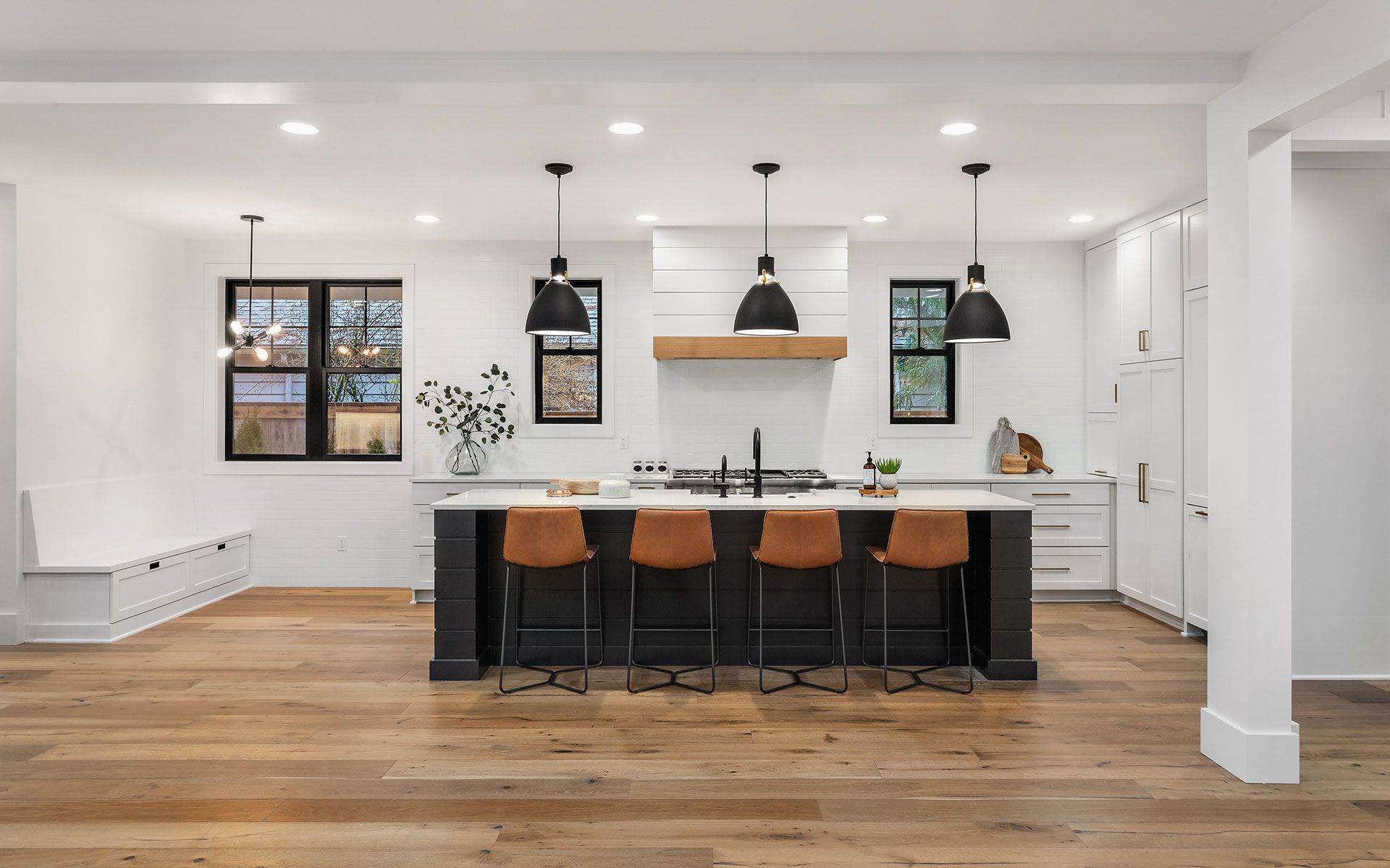 A kitchen with a large island , wooden floors , white cabinets and black stools.