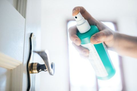 A hand disinfecting a door handle with a spray bottle