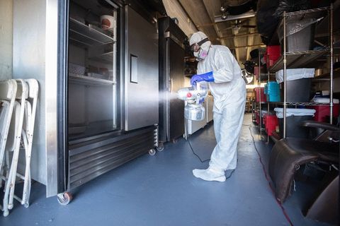 Man in a hazmat suit, spraying the inside of an industrial fridge