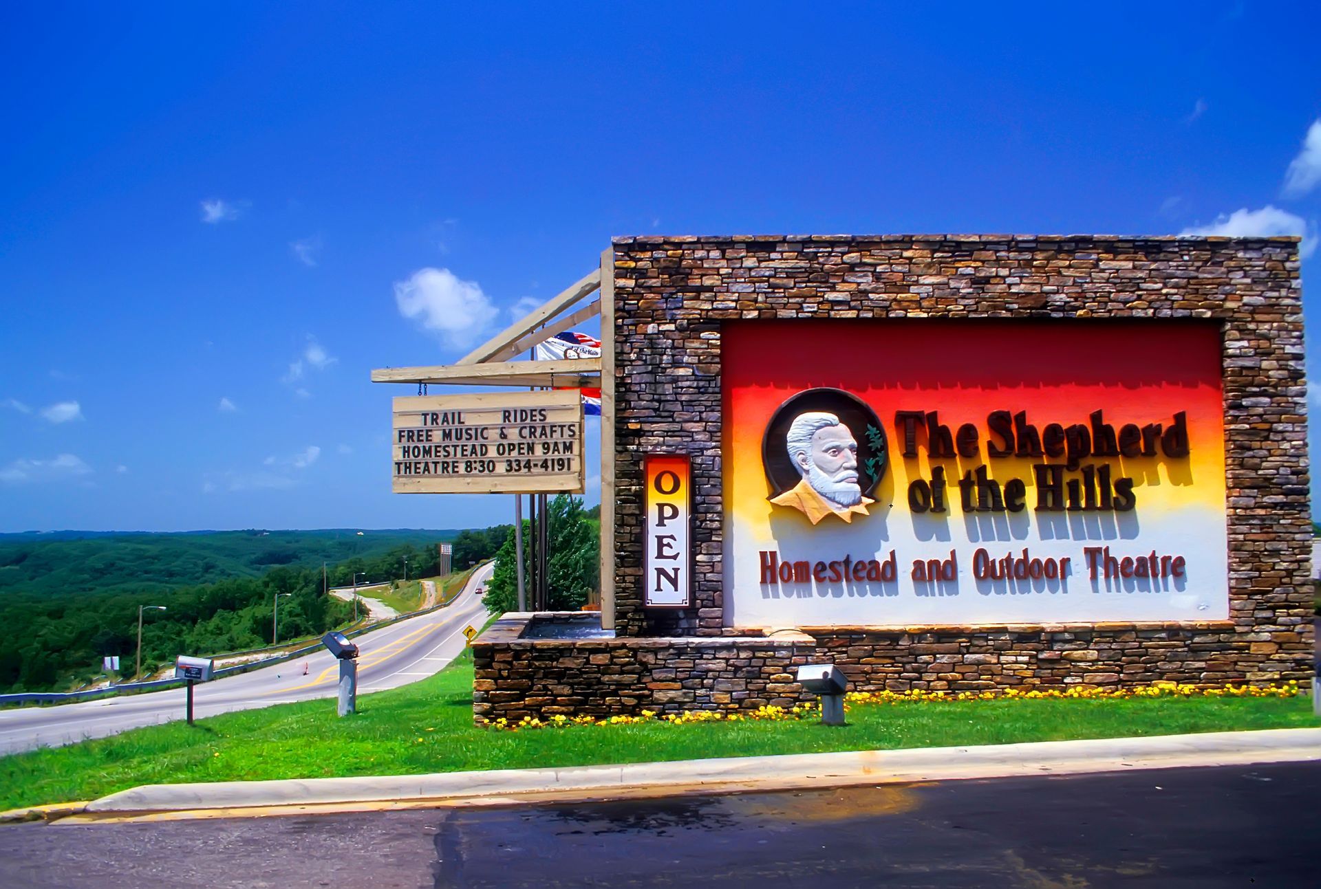 Sign for The Shepherd of the Hills, outdoor theater, with a red background, stone border, and a green landscape.