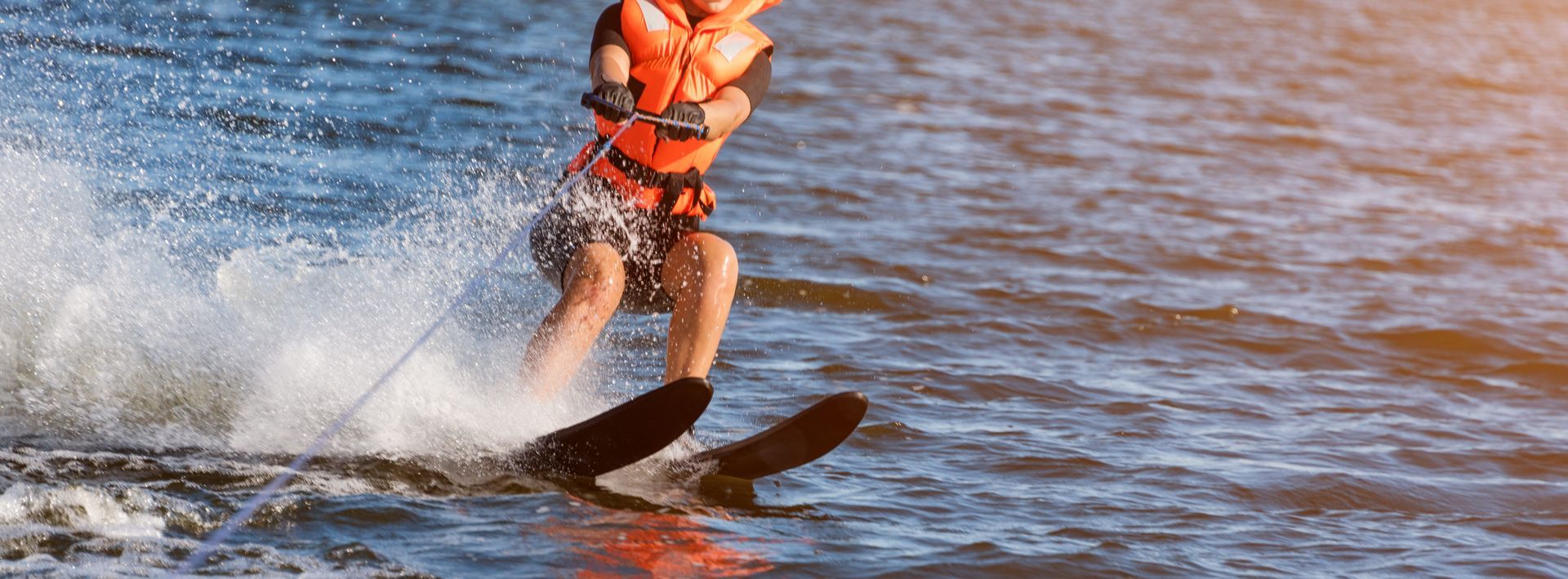 Person water skiing on a lake, wearing a life vest. Water sprays from the skis.