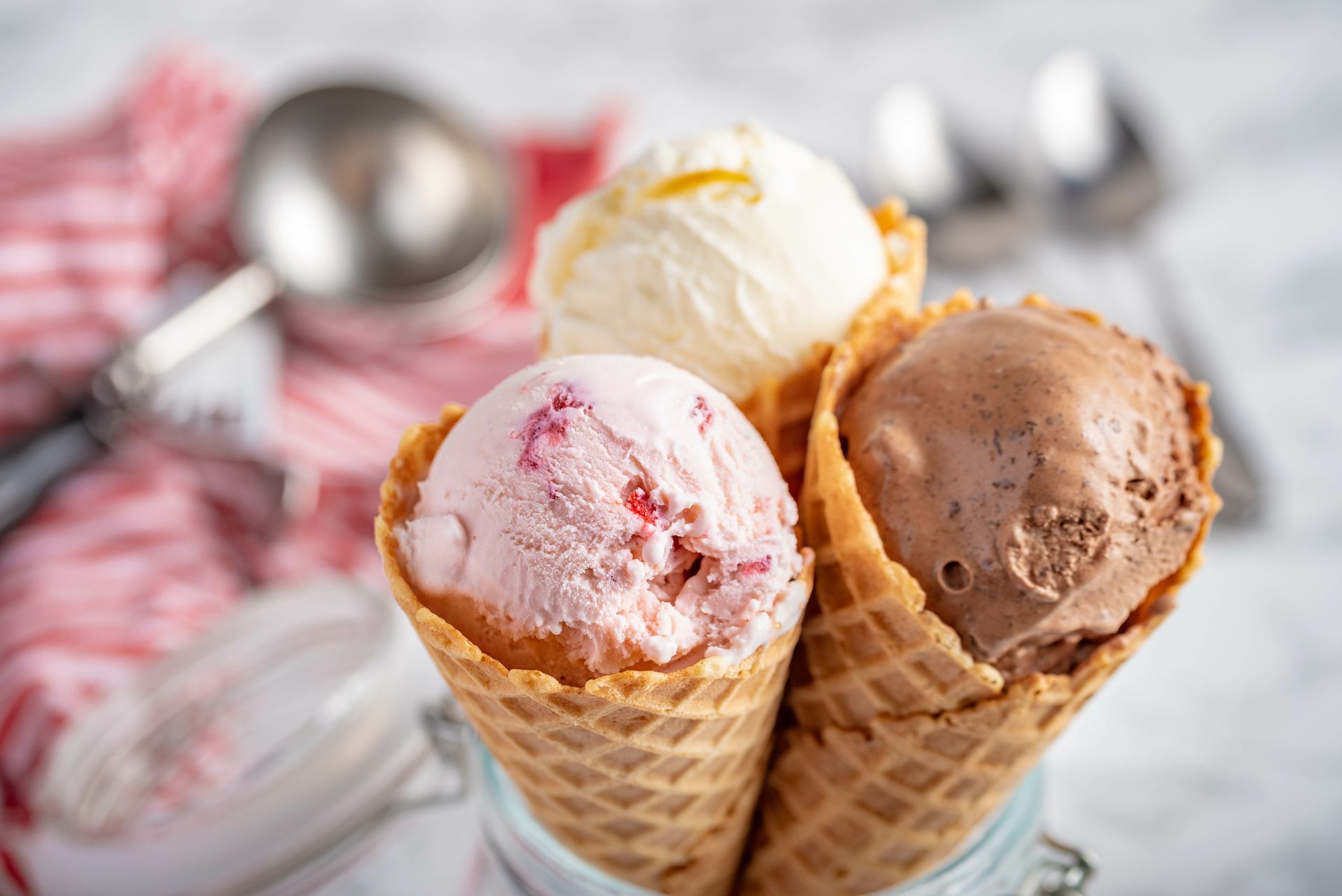 Three scoops of ice cream in waffle cones, including white, strawberry, and chocolate flavors