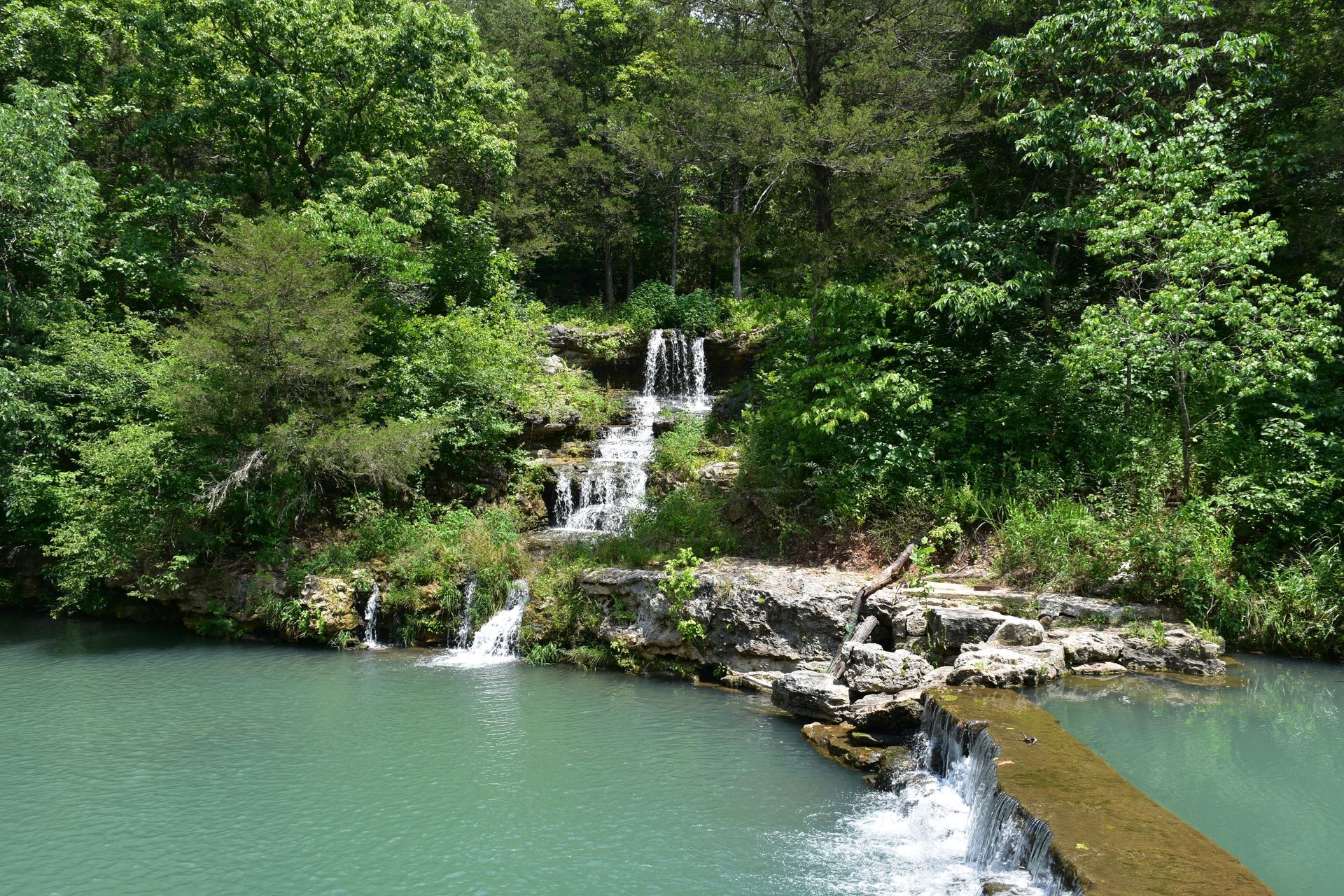 Waterfall cascading into a turquoise pool, surrounded by lush green foliage.